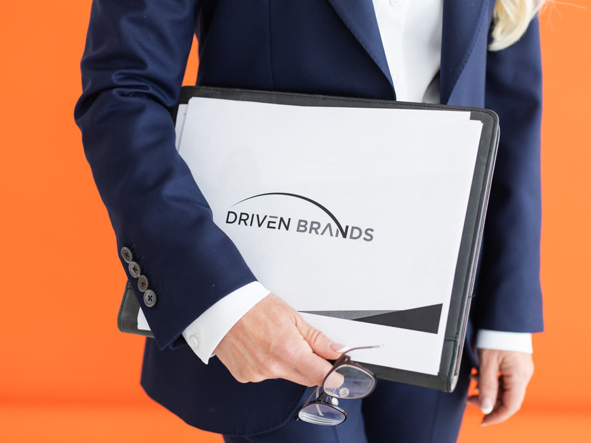 Driven Brands folder held against an orange background
